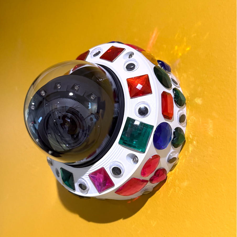 A surveillance camera in Building 10 decorated with decorative gems by faculty protesters.