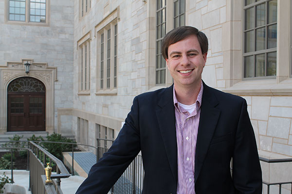 Young man in suit in front of a "Collegiate Gothic" style building. 