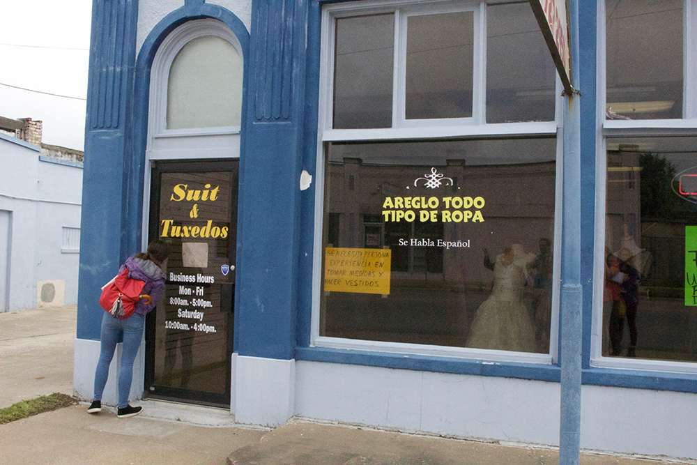 Student peers through door into clothing and alterations shop. 