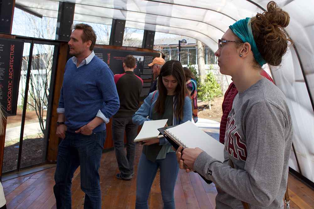 Students sketch in an open structure outdoors with educational materials. 