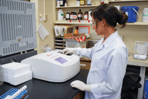 a female student in a lab coat uses a high tech machine