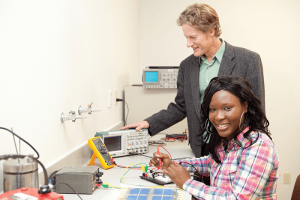 a student and professor work with electrical equipment in a lab