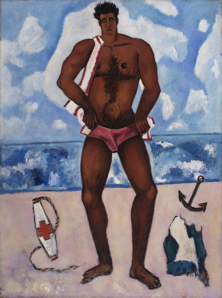 Hartley’s painting “Canuck Yankee Lumberjack at Old Orchard Beach, Maine” depicts a male figure, unclothed except for red swim briefs and a red-and-white striped towel draped over his shoulder, on an idyllic beach scene in Maine. The man’s muscular, solid body is painted in deep shades of reddish brown accented by black paint strokes and outlines, and dominates the central axis of the composition. The background is divided starkly into thirds, each separated by a thin blue brushstroke. The bottom panel depicts a sandy beach, with an anchor, life buoy, and discarded piece of clothing strewn around the figure’s feet. The smaller middle section depicts the ocean with thick, impasto paint ranging from deep blue to white, while the top of the composition features a blue sky with large, floating white clouds. 