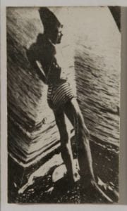 The first image of a young boy in striped bathing trunks. He stands with his hands on his hips and looks outward, surveying the beach.