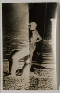 Second image of a young boy in striped bathing trunks. He stands with his hands on his hips and looks outward, surveying the beach.