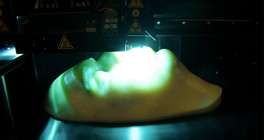 Partially finished 3D print of a lifelike face mask inside the printer