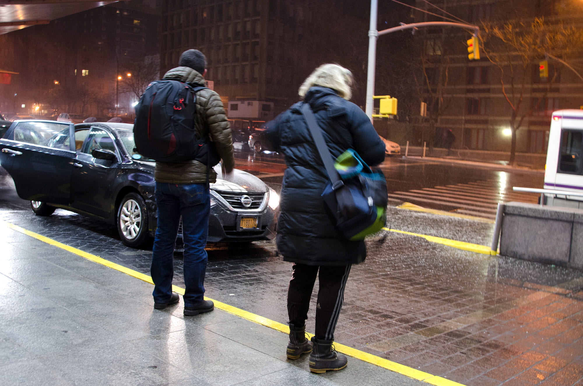 two people standing on the sidewalk while it is snowing