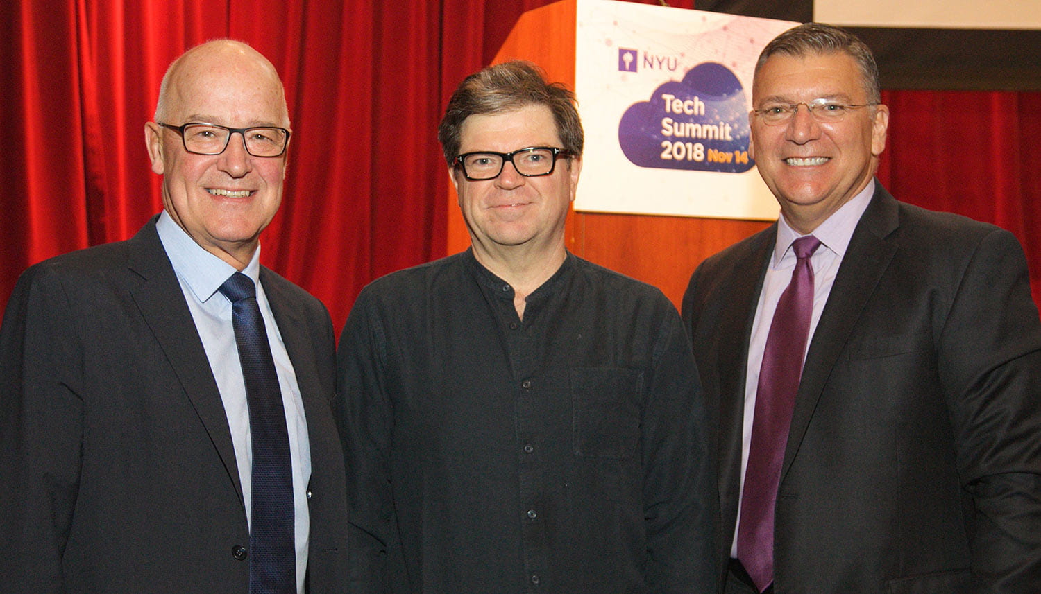 NYU President Andy Hamilton, keynote speaker Yann LeCun, and NYU CIO Len Peters in front of a red curtain at the NYU Technology Summit