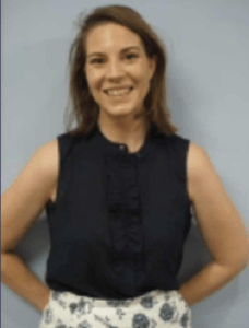 Color portrait of Ashley Grady on a grey background, wearing a black sleeveless shirt and white and blue floral bottoms.