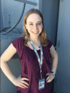 Color portrait of Charlotte Martin on a blue background, wearing a maroon shirt.