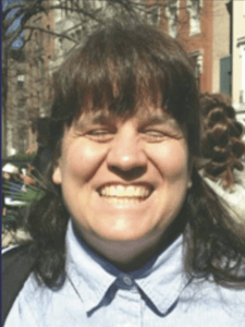 Color portrait of Dr. Cheryl Fogle-Hatch in front of city street, wearing a blue button down shirt.