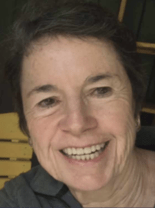 Color portrait of Ellen Giusti on a black background, wearing a grey collared shirt.