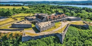 Fort building on top of hill surrounded by trees with a river in the background.