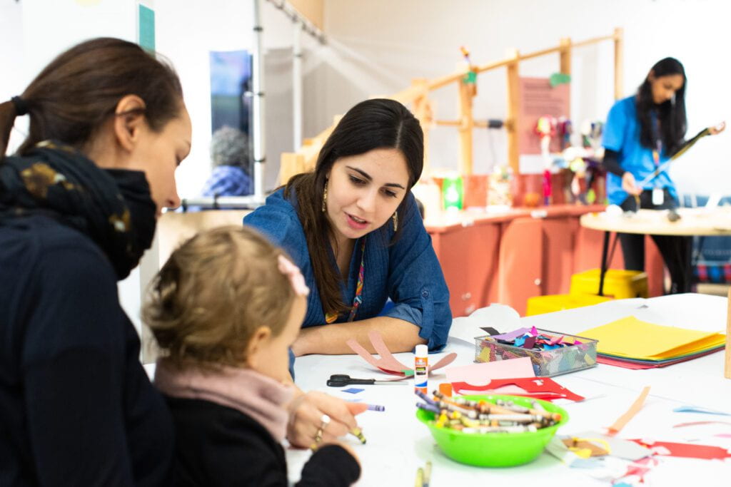 two adults and a child sit around a table with art materials