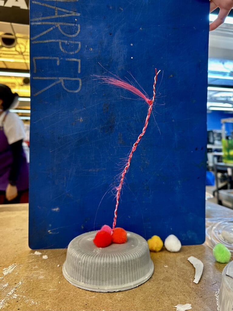 A work in progress picture of the object with concrete base with pompoms, and the wire stem.