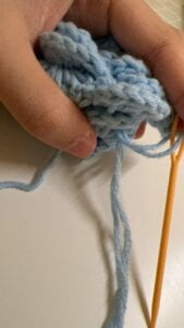 My hand holding the chunk of crocheted yarn that will be curled and consist the flower head