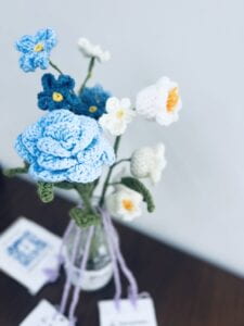 Three crocheted flowers in a glass bottle, with three QR codes tied to each of their stems