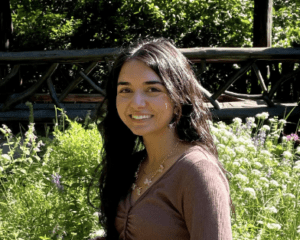 Brunette woman wearing a brown shirt standing in a garden