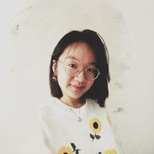 A asian female with short, black hair at her shoulders, wearing glasses and a sunflower sweater, smiling at the camera