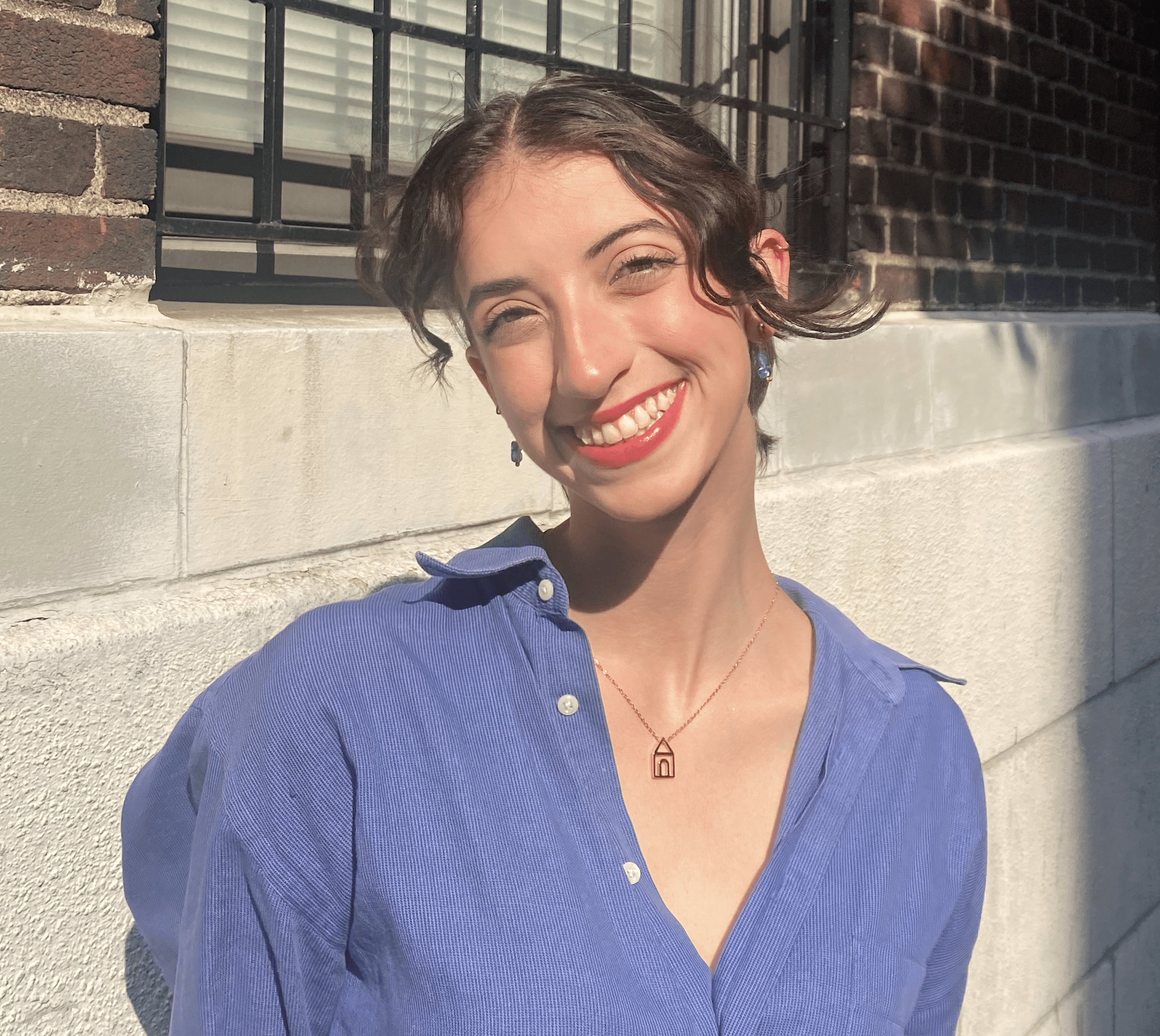 Stephanie a mixed race white passing young woman smiles in warm sunlight. She wears a blue button down.