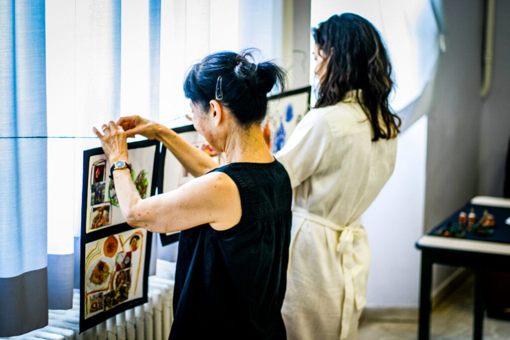 Ikuko stands next to a student and hangs her work.