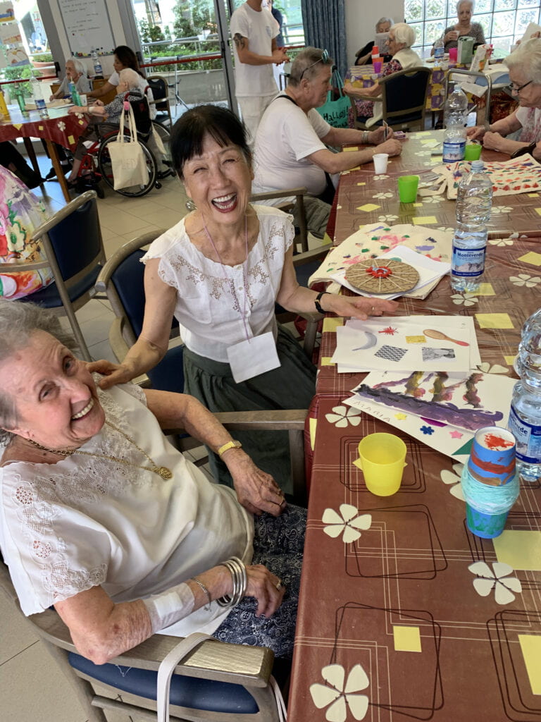 Ikuko and a student sit together at a table and laugh joyously.