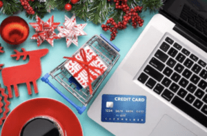 holiday themed image showing open laptop with credit card near track-pad, coffee and holiday themed items are visible near the laptop