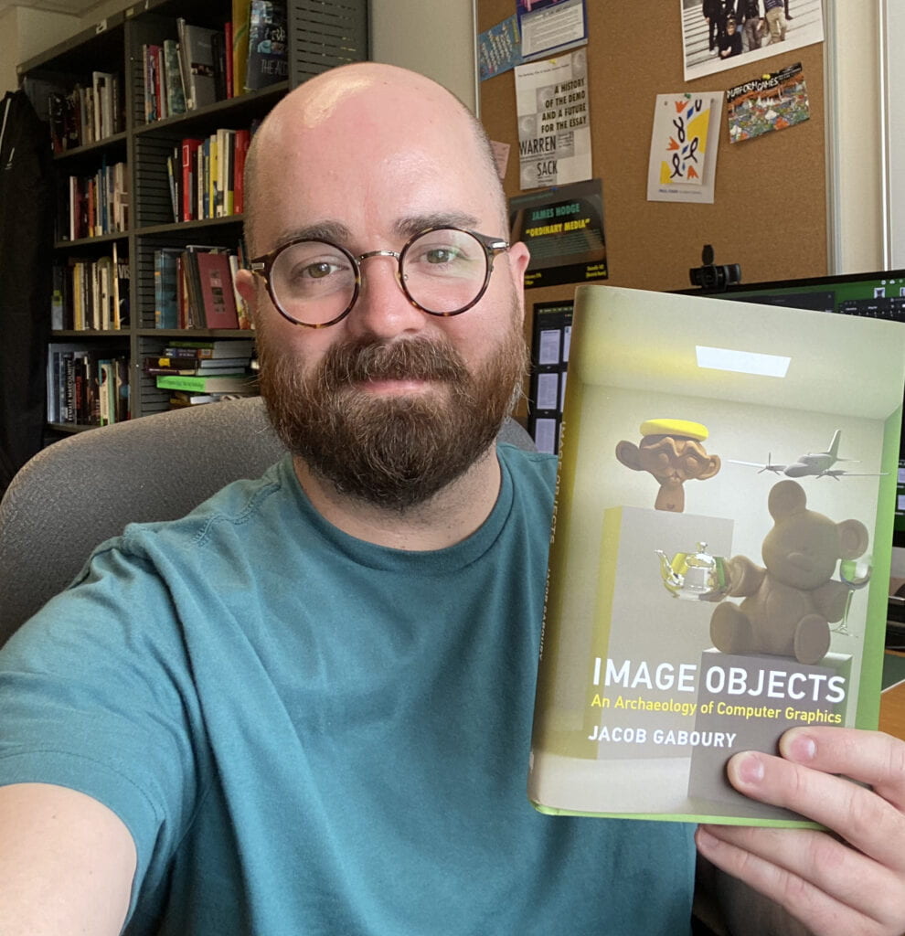 PhD alum Jacob Gaboury holds a copy of his book, Image Objects