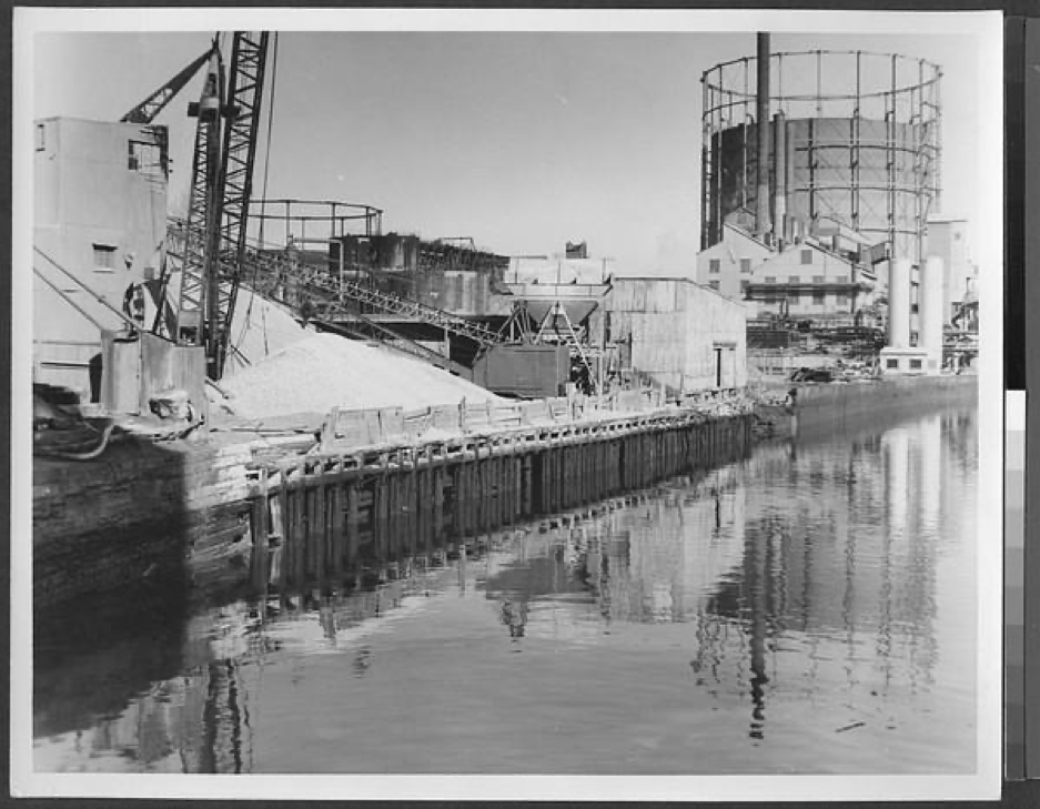 View of Gowanus Canal looking east. Industrial structures along the bank include storage sheds, warehouses, smoke stacks, gravel pits, and water or gas tanks. Credit: Irving I. Herzberg photograph collection, Brooklyn Public Library, Center for Brooklyn History