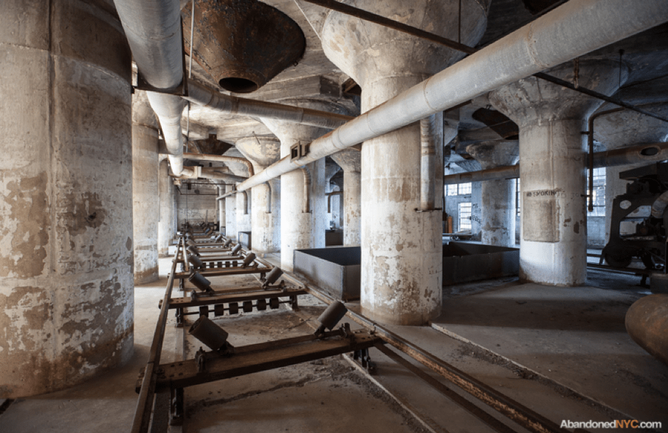 Interior view of abandoned Red Hook Grain Terminal, showing grain funnels penetrating floor slab with conveyance tracks beneath. Credit: Will Ellis, AbandonedNYC