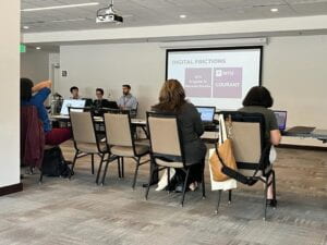 From left to right, Jeff, Rosanna, and Craig sit at the front of a classroom. To the right is a large projection screen displaying a powerpoint slide titled "Historic Fractures." A small audiences sits in front of the screen. 