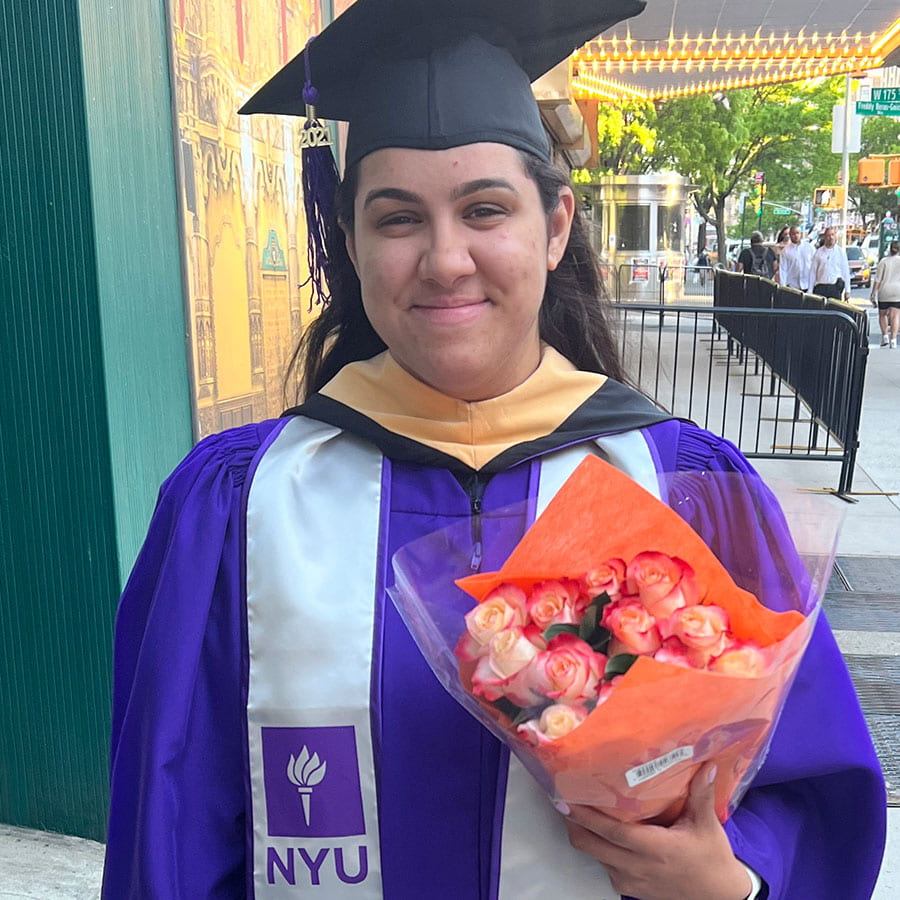 Arlys Tineo wearing NYU graduation attire and holding flowers