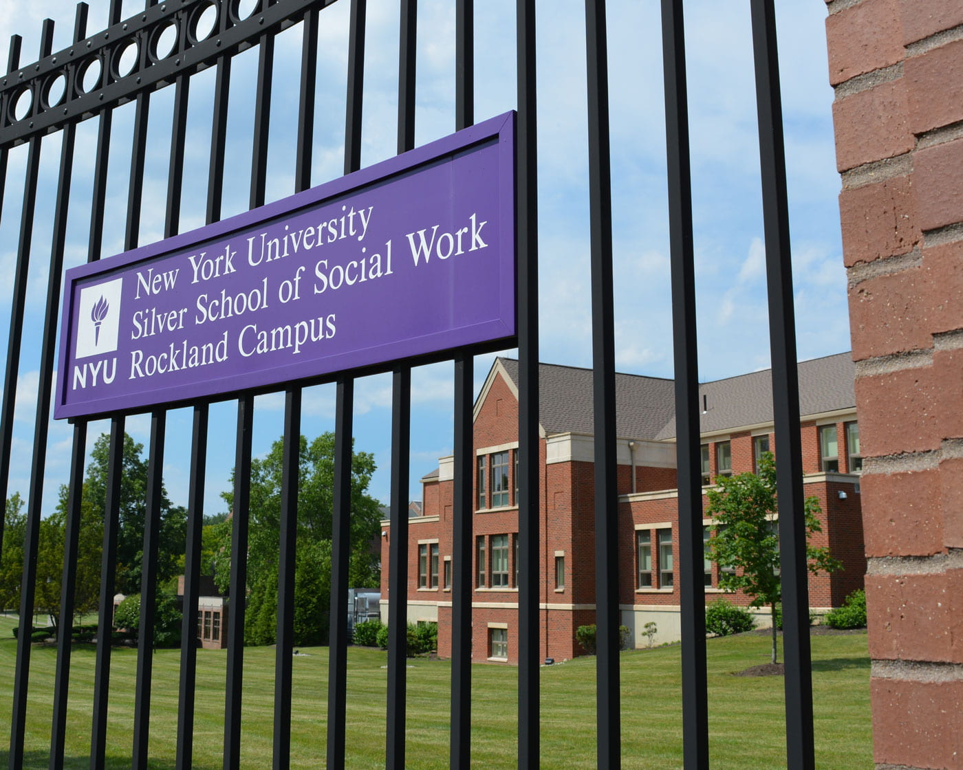 Rockland campus building behind an iron fence with a violet sign with the NYU logo and the text New York University Silver School of Social Work Rockland Campus