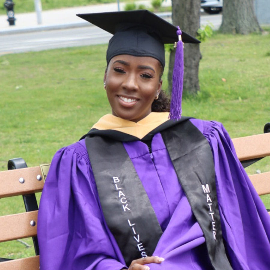 Sheryl Hugh sitting on a bench wearing graduation attire