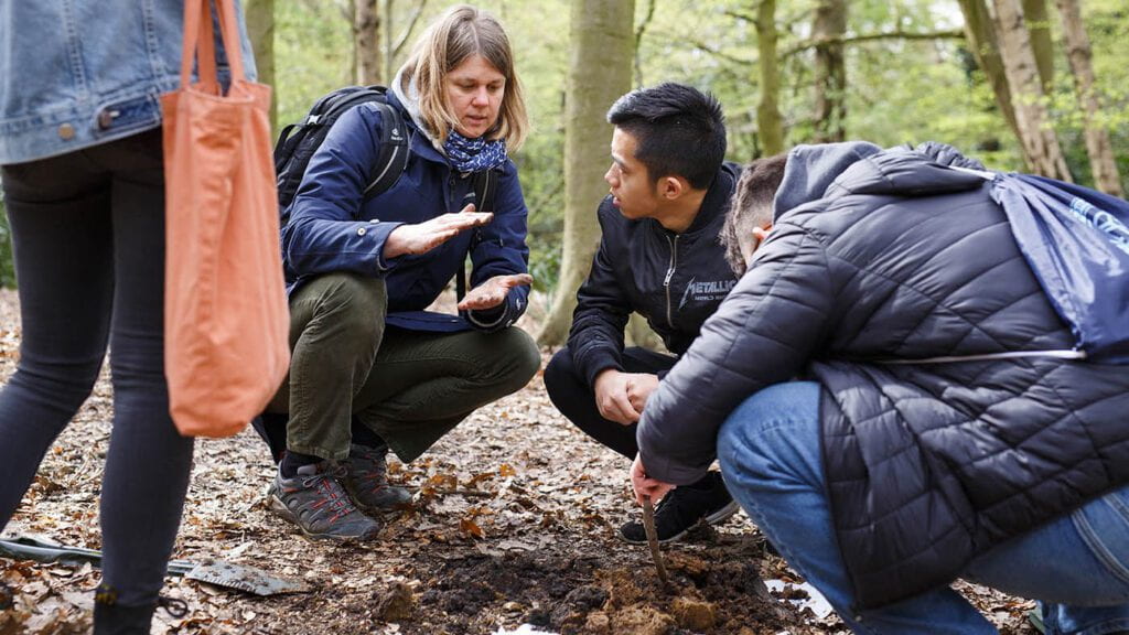 A professor and students squat in the forest to discuss the soil