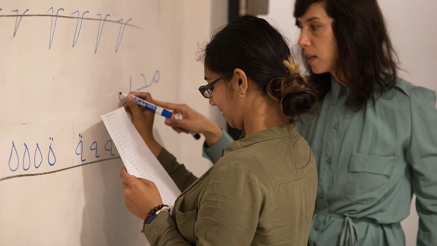 A teacher instructs a student writing letters on a whiteboard