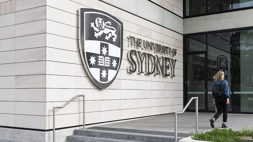 A student walks into a building with a larger University of Sydney sign