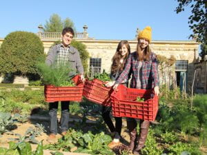 Three students holding bins filled with green vegetables smiling at the camera