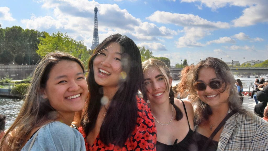 Four students posing for the camera with the Eiffel Tower visible in the background.