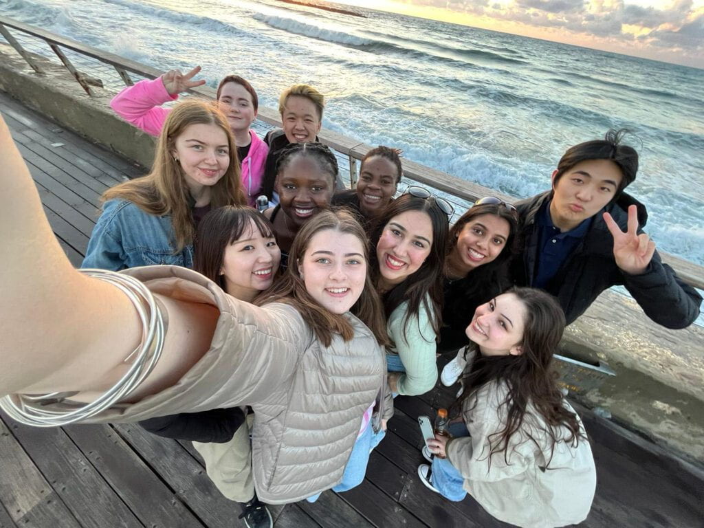 A group of students pose for a selfie with the ocean in the background