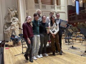 Seven people pose for a camera on the orchestra stage