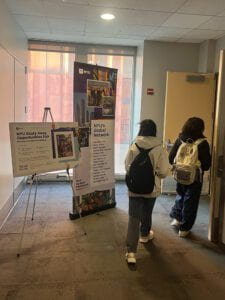 Two students with backpacks walk past signs for the fair