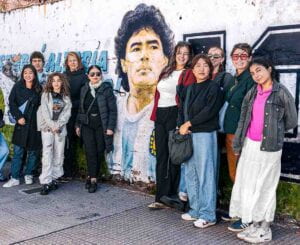 A group of students stand in front of a street mural featuring Argentinian soccer player Diego Maradona