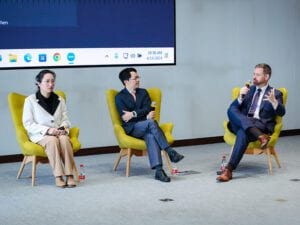 Jin Han, Yang Feng, and Brian Hall seated in chairs in discussion