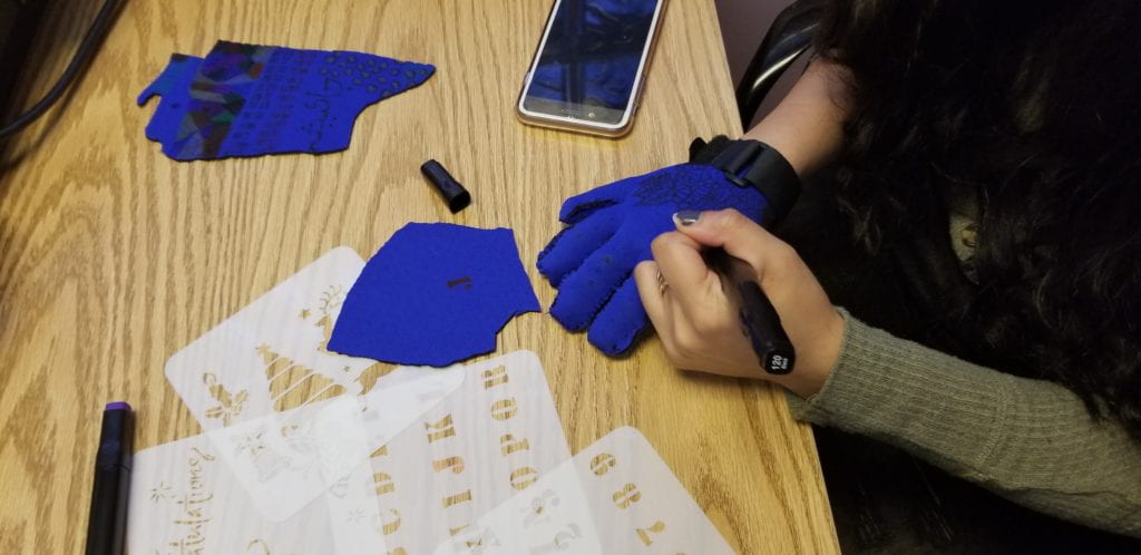 THE PATIENT IS DRAWING ON THE DORSAL PART OF THE GLOVE USING STENCILS AND FABRIC PAINT MARKERS