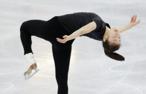 A female-presenting figure skater, dressed in black, does a camel spin.