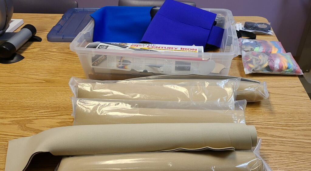 Image of beige felt neoprene rolls and blue cloth neoprene in a plastic box with black iron on seam tape and velcro rolls