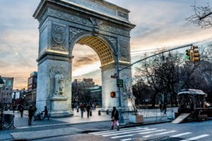 Sun setting on Washington Square Arch with a diverse group of people in the park.