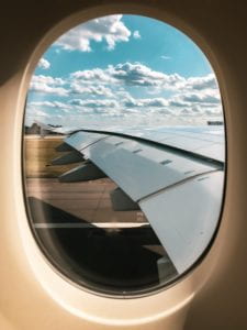 A passenger's window overlooking the airplane's wing and a cloudy sky on an airplane runway