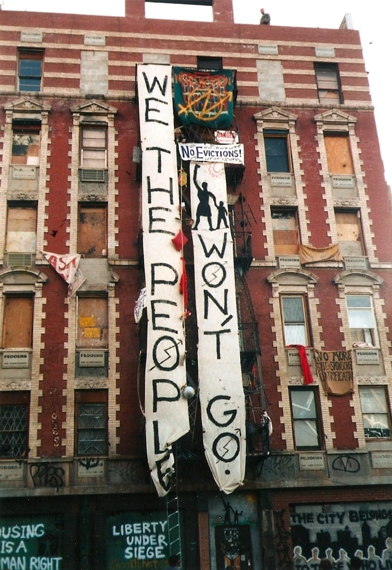 Banner hanging from a tenement building that reads, "We the People Won't Go."